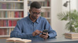 © stockbakers - Young African Man using Smartphone in Office