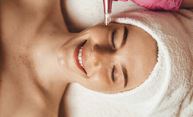 Wall Mural - beautiful attractive female patient smiling while receiving face oxygen peeling at spa salon. health