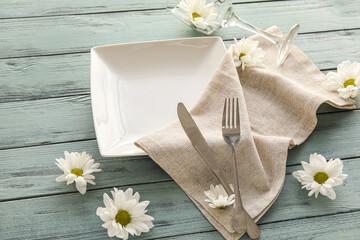 Table setting with beautiful chamomile flowers on color wooden background