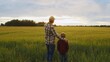 © Acronym - Farmer and his son in front of a sunset agricultural landscape. Man and a boy in a countryside field. Fatherhood, country life, farming and country lifestyle.