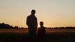 © Acronym - Farmer and his son in front of a sunset agricultural landscape. Man and a boy in a countryside field. Fatherhood, country life, farming and country lifestyle.