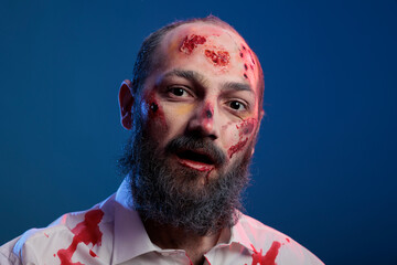Fototapeta portrait of undead scary zombie man posing with bloody scars and spooky halloween costume looking dangerous and apocalyptic. horror aggressive deadly monster corpse eating brain.