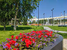 Noyabrsk, Russia - June 21, 2022: Beautiful View Of A Flower Bed With Red Begonia Flowers And A Town Square With A Fountain And A Swing On A Sunny Summer Day
