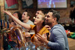 © gpointstudio - Multiracial group of friends cheering of soccer fans in the pub
