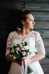 Wall Mural - Young beautiful bride in elegant dress is standing and holding hand bouquet of white flowers and greens with ribbon.