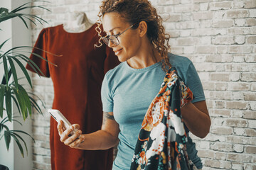 Modern female seamstress calling and using mobile phone at the workshop working with clothes and fashion business. One happy woman people work as a tailor with red dress in background. Lady smile