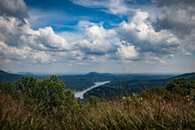 A View Towards Lake Lure From The Pick Of Chimney Rock In North Carolina With Gorgeous Puffy Clouds Above It And Dry, Long Steams Of Grass On The Foreground