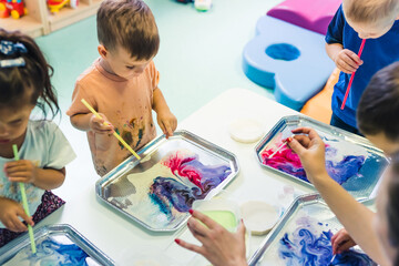 Wall Mural - Multi-cultural nursery school. Toddlers playing with striped straws and milk painting, using nontoxic food coloring for colors. Creative kids activity for using their senses and brain development