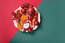 Christmas And New Year Holiday Background. Christmas Decorations With Santa Claus Ginger Cookies, Tangerines, Nuts, Balls, Candy Canes On Red-green Backdrop. Symbol Of Festive Winter Season. Top View