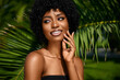 © Beauty Agent Studio - Tropical beauty portrait of young African American model with curly hair touching her chin and  posing against green palms leaves. Natural cosmetics skin care concept