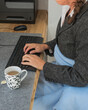 Eine Frau schützt sich mit Decke und heißem Tee am Schreibtisch vor der Kälte bei der Arbeit, Konzept Energiekosten, Energiesparen durch Absenken der Raumtemperatur