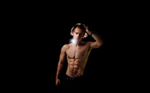 Muscular Athletic Man With A Naked Torso And Inflated Abdominal Muscles On A Black Background. Sexy Man With Long Hair.