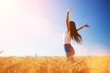 Happy woman enjoying the life in the field. Nature beauty, blue sky, white clouds and field with golden wheat. Outdoor lifestyle. Freedom concept. Woman jump in summer field