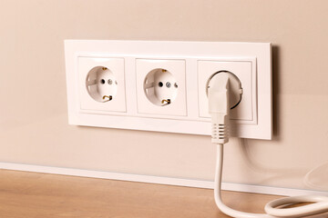 Group of white european electrical outlets with plug inserted into it on modern beige wall. Selective focus