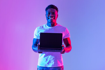 Check this website. Handsome young black man holding laptop with blank screen in neon light, mockup for design