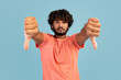 © Prostock-studio - Unhappy handsome young eastern guy showing thumbs down on blue