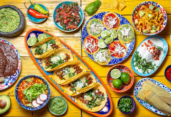 Mexican festive food for independence day independencia - chiles en nogada, tacos al pastor, chalupas pozole, tamales, chicken with mole poblano sauce. Yellow background.