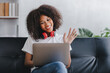 © Daenin - african american woman sitting on sofa at home video call chatting with friends using a laptop and a smartphone or phone