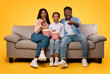 © Prostock-studio - Overjoyed african american family watching movie and eating popcorn from buckets, parents sitting with daughter on couch