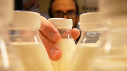 Close-up of milk bottles on a dairy departments shelf and a male buyer takes one