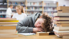 Portrait Of A Tired Fifteen-year-old Schoolboy Who Fell Asleep On A Desk Among Textbooks In The School Library