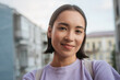 © Maria Vitkovska - Smiling asian tourist taking selfie outdoors. Beautiful Korean woman wearing purple casual t shirt looking at camera standing on the street