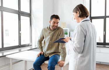 Poster - medicine, healthcare and people concept - female doctor with clipboard and happy smiling man patient meeting at hospital