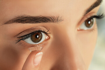 Wall Mural - Young woman putting contact lens in her eye, closeup