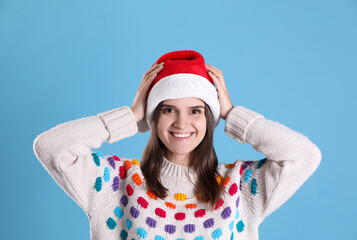 Poster - Pretty woman in Santa hat and festive sweater on light blue background