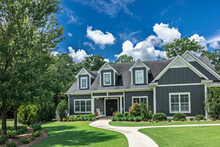 A Large Gray Craftsman New Construction House With A Landscaped Yard And Leading Pathway Sidewalk