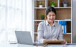 © crizzystudio - Young woman working on a laptop in the office. Asian businesswoman sitting at her workplace in the office.  Beautiful Freelancer Woman working online at her home.