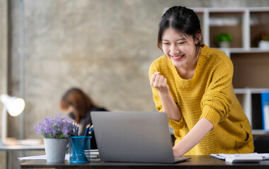 Asian businesswoman rejoicing and raising her hand, working and using a laptop Document graph showing the results in the meeting room.