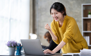 Asian businesswoman rejoicing and raising her hand, working and using a laptop Document graph showing the results in the meeting room.