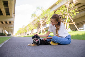 Happy young asian woman playing and sitting on road in the park with her dog. Pet lover concept