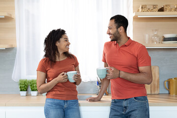 Wall Mural - Happy relaxed young african american guy and woman in same red t-shirts with cups enjoy drink and free time