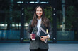 © Strelciuc - Beautiful Caucasian businesswoman holding laptop computer and take away hot drink standing outside company building. Lifestyle and work concept. Looking at