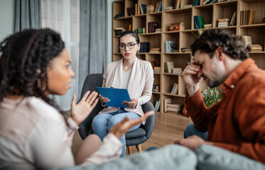 Wall Mural - Calm european millennial female psychologist consults quarreling multiracial husband and wife