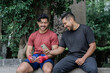 © Daniel - Two Latino men sitting on a park bench smiling and looking at the phone.
