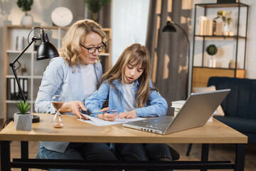 Young caucasian mother helping daughter remote studying at home explaining doing homework together. Parent mom teaching teenage school child distance learning online virtual class on computer.