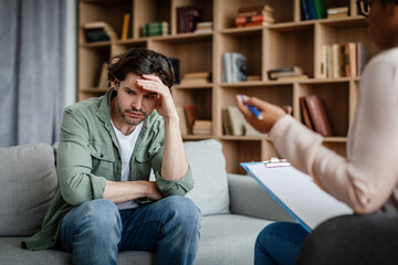 Wall Mural - Unhappy depressed young european male patient listens to black woman psychologist in clinic interior