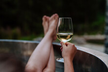 Unrecognizable Young Woman With Feet Up Relaxing With Glass Of Wine In Hot Tub Outdoor In Nature.