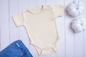 Wall Mural - Yellow baby bodysuit mockup for logo, text or design on wooden background with pumpkins top view