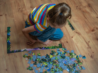 A beautiful little girl assembles a complex puzzle on a wooden floor.