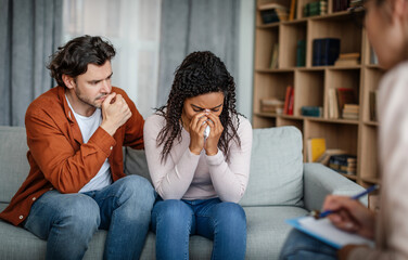 Wall Mural - Despaired sad young european man calms black crying woman at meeting with psychologist in office