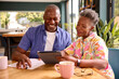 Smiling Senior Couple Sitting Around Table At Home Reviewing Finances Using Digital Tablet