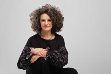 Portrait of senior woman with lush curly hair and black pantsuit posing in studio