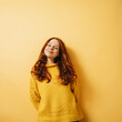 © contrastwerkstatt - smiling redhead woman with yellow sweater looks at camera, copyspace against yellow backgroun