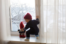 Baby Boy Sitting With Soft Toy Gnome On The Window