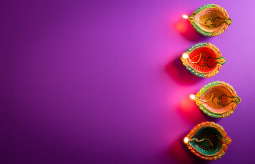 Happy Diwali - Clay Diya lamps lit during Dipavali, Hindu festival of lights celebration. Colorful traditional oil lamp diya on purple background