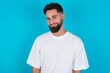 © Jihan - Happy bearded caucasian man wearing white T-shirt over blue background looking at camera with charming cute smile.